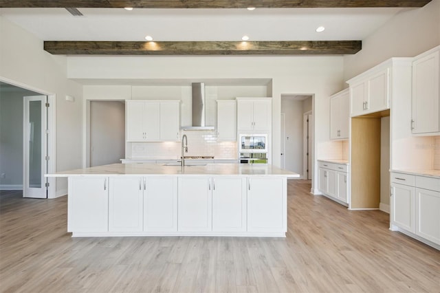 kitchen featuring decorative backsplash, beam ceiling, wall chimney exhaust hood, and a center island with sink