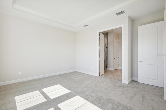 unfurnished bedroom with visible vents, light carpet, ornamental molding, and a raised ceiling