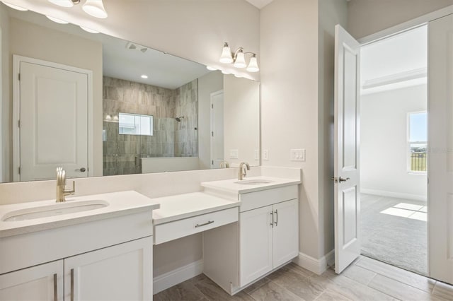 bathroom with vanity, baseboards, a tile shower, and a healthy amount of sunlight