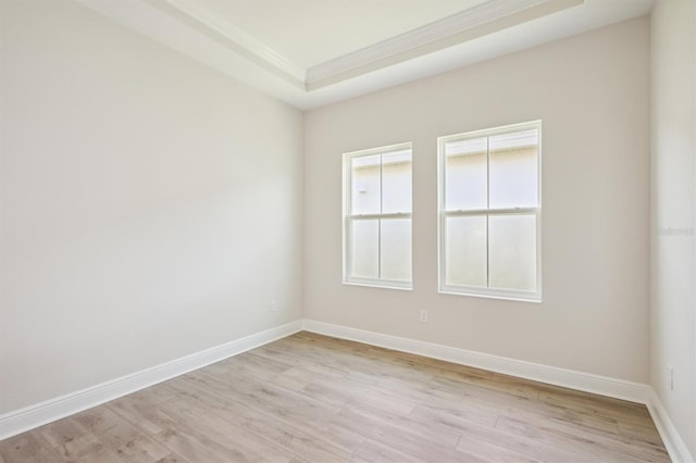 empty room with light wood-style floors, baseboards, ornamental molding, and a raised ceiling