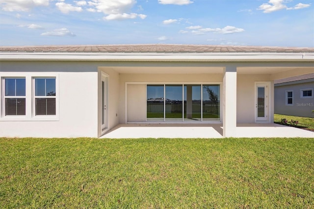 back of house with a lawn, stucco siding, and a patio area