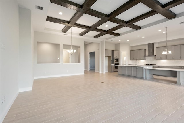 unfurnished living room with coffered ceiling, sink, beam ceiling, an inviting chandelier, and light hardwood / wood-style flooring