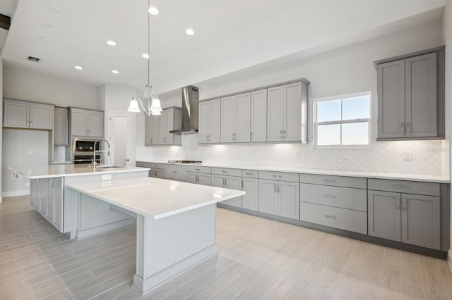 kitchen with gas cooktop, stainless steel microwave, wall chimney exhaust hood, and an island with sink