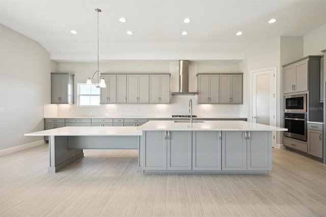 kitchen with gray cabinetry, a large island, wall chimney range hood, and stainless steel appliances