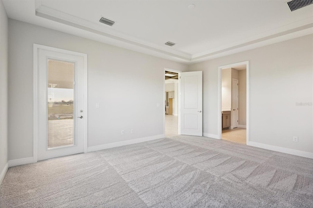 unfurnished bedroom with a raised ceiling, ensuite bathroom, and light colored carpet