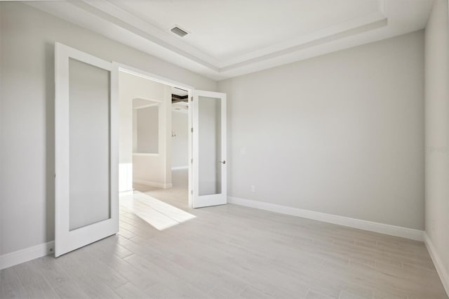 unfurnished room with a tray ceiling, french doors, and light hardwood / wood-style floors