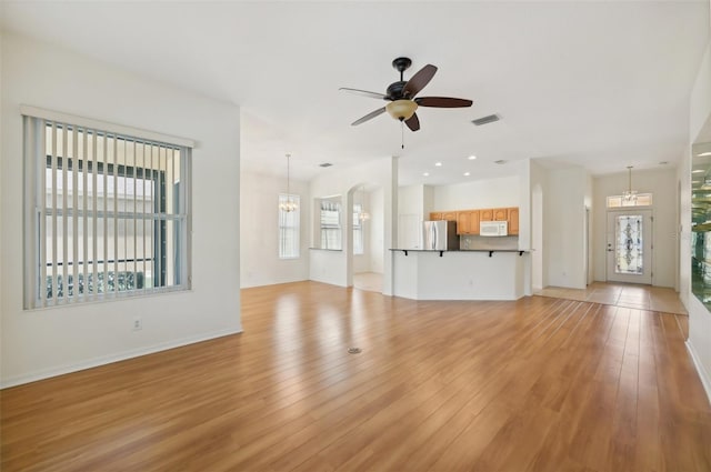 unfurnished living room with ceiling fan with notable chandelier and light hardwood / wood-style floors