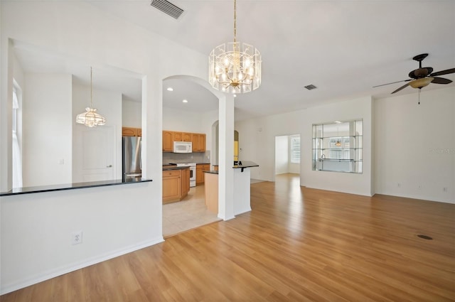 unfurnished living room with ceiling fan with notable chandelier and light wood-type flooring