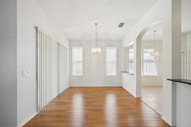 unfurnished dining area featuring a wealth of natural light, light hardwood / wood-style flooring, and a chandelier