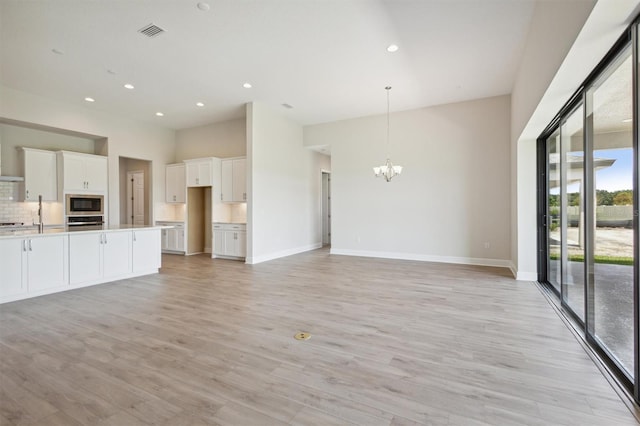 unfurnished living room with light wood-type flooring and an inviting chandelier