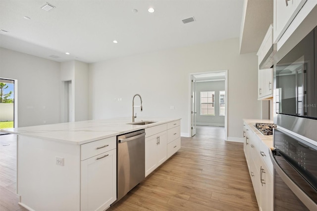 kitchen with appliances with stainless steel finishes, a center island with sink, sink, and light hardwood / wood-style floors