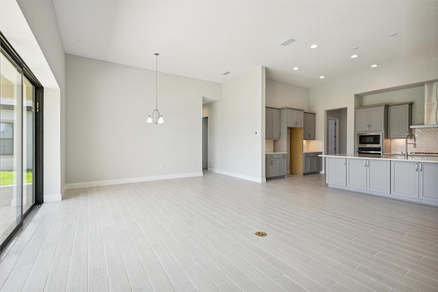 kitchen with gray cabinets, light hardwood / wood-style flooring, pendant lighting, and backsplash