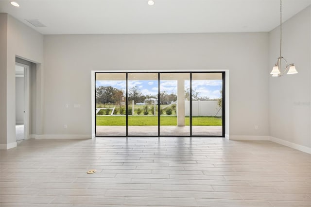 spare room with a notable chandelier, light wood-type flooring, and a wealth of natural light