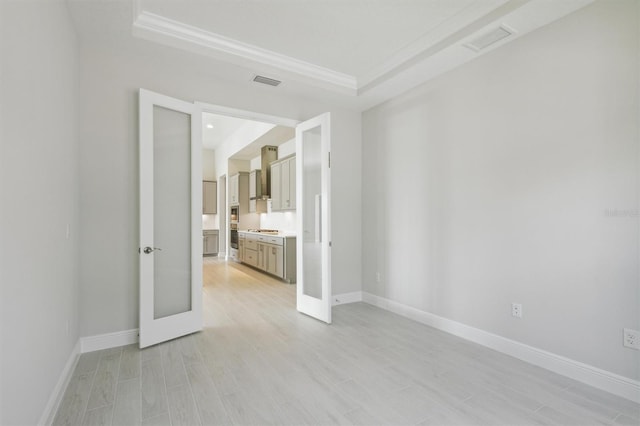 spare room featuring light hardwood / wood-style floors, french doors, and a raised ceiling