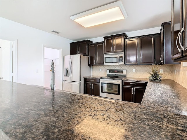 kitchen with backsplash, dark stone counters, dark brown cabinetry, and stainless steel appliances