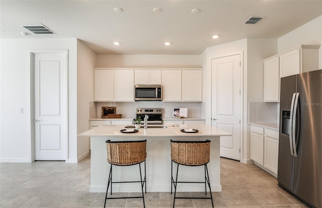 kitchen featuring tasteful backsplash, light tile patterned floors, an island with sink, stainless steel appliances, and white cabinets