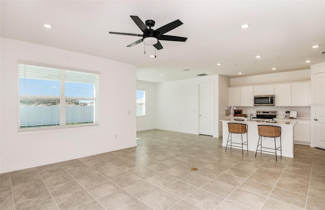 kitchen with ceiling fan, white cabinetry, an island with sink, a breakfast bar area, and stainless steel appliances