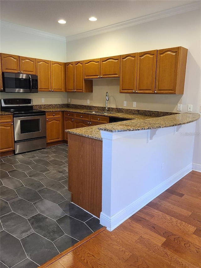 kitchen featuring dark stone counters, stainless steel appliances, ornamental molding, dark hardwood / wood-style floors, and kitchen peninsula