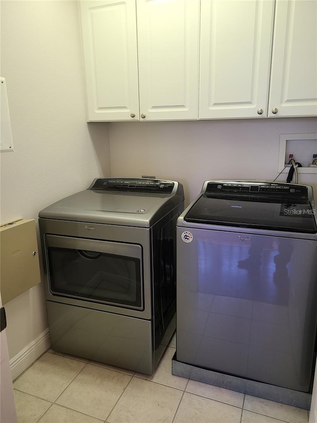 clothes washing area with washing machine and clothes dryer, cabinets, and light tile patterned floors