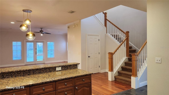 kitchen with hardwood / wood-style floors, crown molding, hanging light fixtures, and dark stone countertops