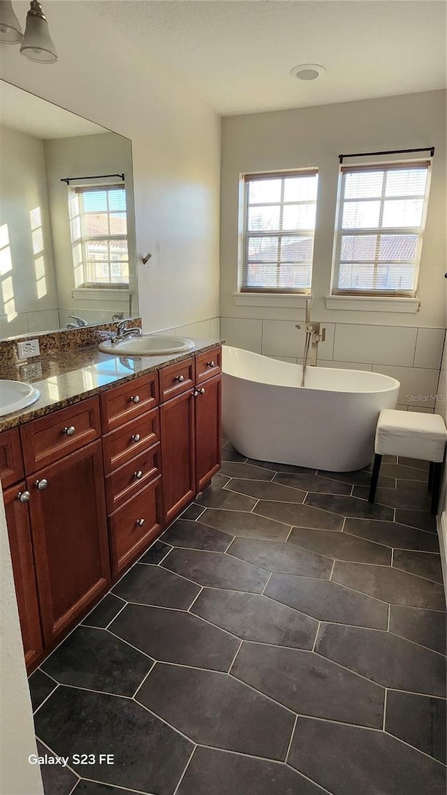 bathroom featuring vanity, a bath, and tile walls