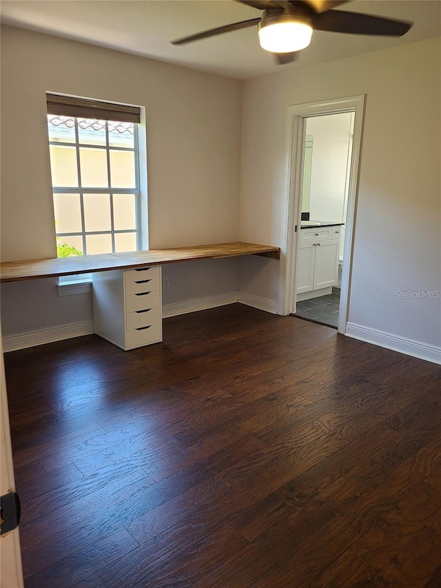 empty room with ceiling fan, dark hardwood / wood-style flooring, and built in desk