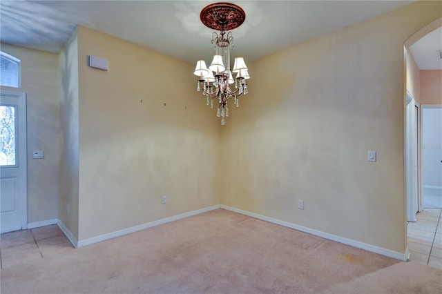 spare room featuring a chandelier and light carpet