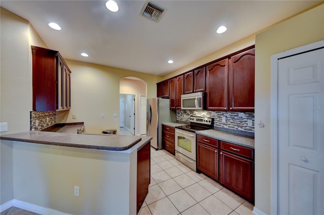 kitchen featuring backsplash, light tile patterned flooring, kitchen peninsula, and appliances with stainless steel finishes