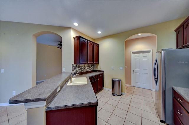 kitchen with light tile patterned floors, sink, stainless steel refrigerator, backsplash, and kitchen peninsula