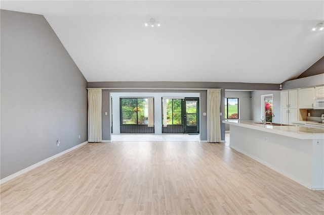 unfurnished living room with high vaulted ceiling, light wood-style floors, baseboards, and a sink