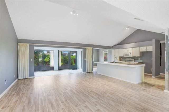 interior space featuring a center island with sink, range with electric stovetop, sink, light wood-type flooring, and high vaulted ceiling