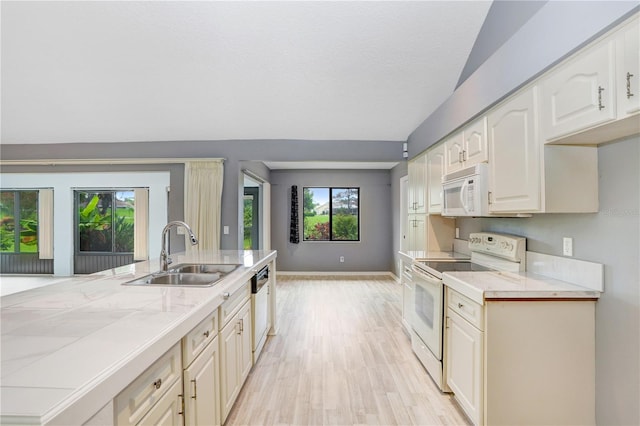 kitchen with white appliances, vaulted ceiling, sink, light hardwood / wood-style floors, and tile counters