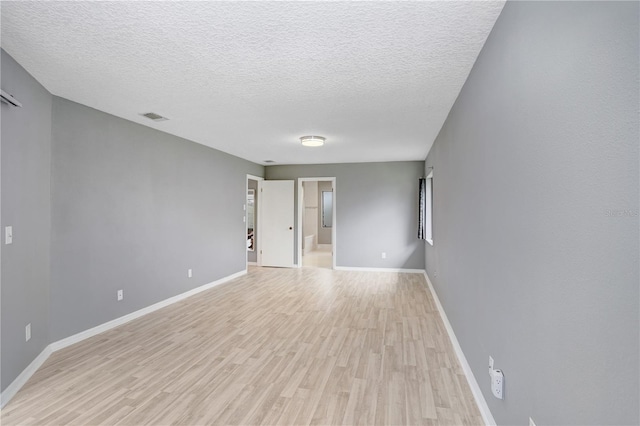 spare room featuring light wood-type flooring, baseboards, visible vents, and a textured ceiling