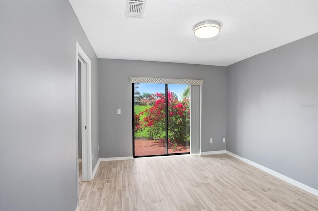 spare room with light wood-type flooring, visible vents, a textured ceiling, and baseboards