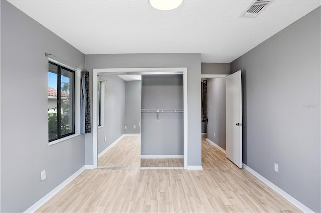 unfurnished bedroom with a closet, wood finished floors, visible vents, and baseboards