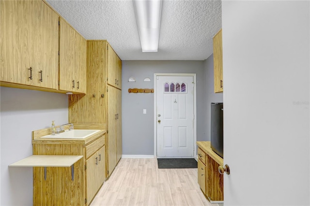 interior space with baseboards, a sink, a textured ceiling, and light wood finished floors