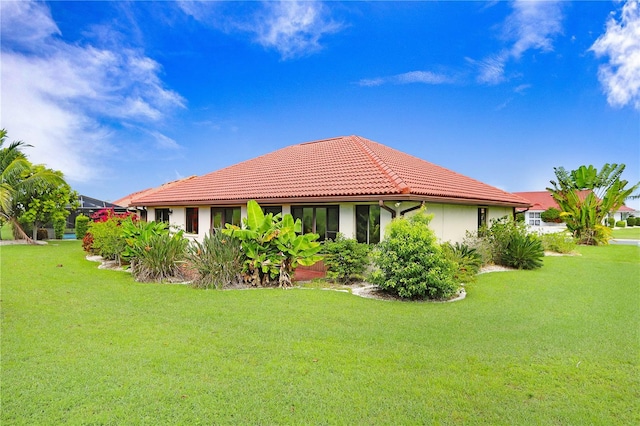 rear view of house featuring a tiled roof, a lawn, and stucco siding