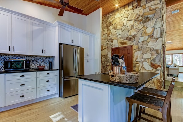 kitchen with a breakfast bar area, white cabinetry, wooden ceiling, stainless steel refrigerator, and a kitchen island