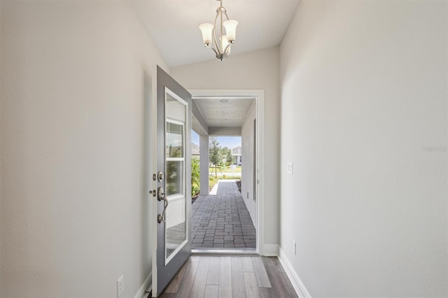 entryway featuring vaulted ceiling, wood-type flooring, and a chandelier