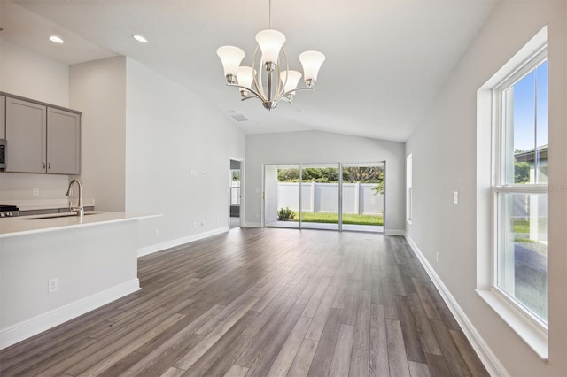 unfurnished living room featuring baseboards, dark wood finished floors, lofted ceiling, an inviting chandelier, and a sink