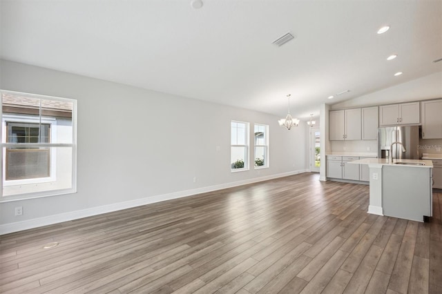 unfurnished living room with baseboards, visible vents, wood finished floors, vaulted ceiling, and a notable chandelier