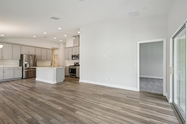 kitchen featuring visible vents, an island with sink, open floor plan, stainless steel appliances, and light countertops