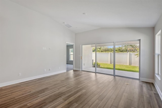 empty room with lofted ceiling, plenty of natural light, baseboards, and wood finished floors