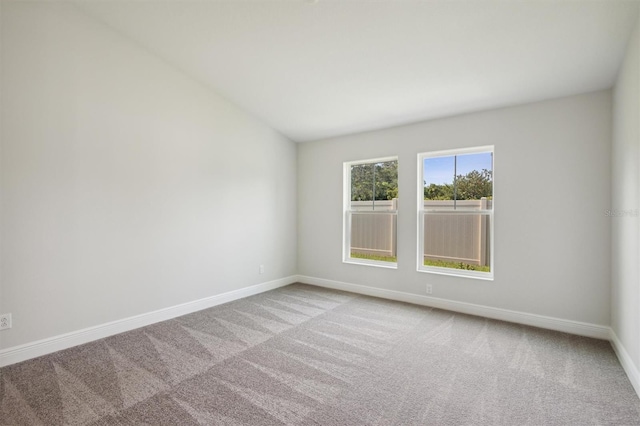 carpeted spare room with lofted ceiling and baseboards