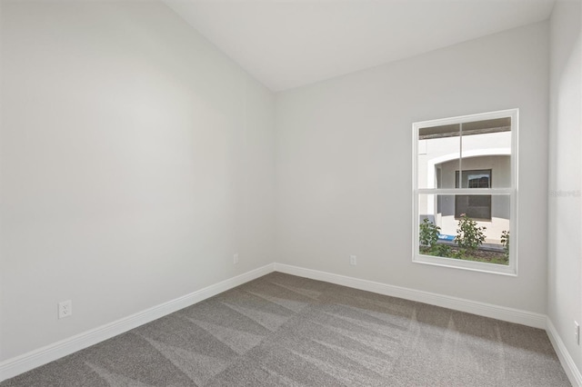 carpeted spare room featuring lofted ceiling and baseboards