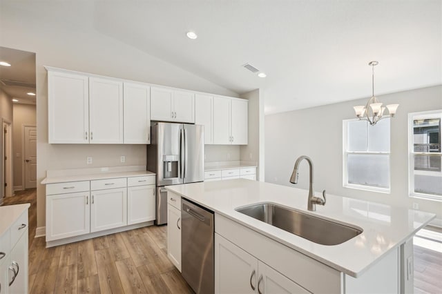 kitchen with a sink, light countertops, appliances with stainless steel finishes, hanging light fixtures, and a center island with sink