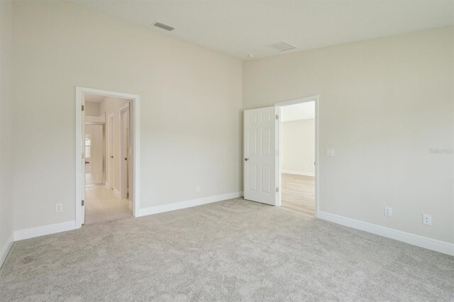 unfurnished bedroom featuring light carpet, high vaulted ceiling, baseboards, and visible vents