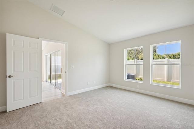 empty room featuring lofted ceiling, baseboards, visible vents, and light colored carpet