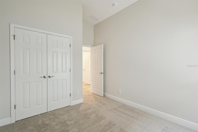 unfurnished bedroom featuring high vaulted ceiling, a closet, light carpet, and baseboards