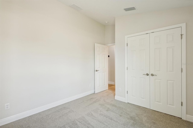 unfurnished bedroom featuring light colored carpet, a closet, visible vents, and baseboards